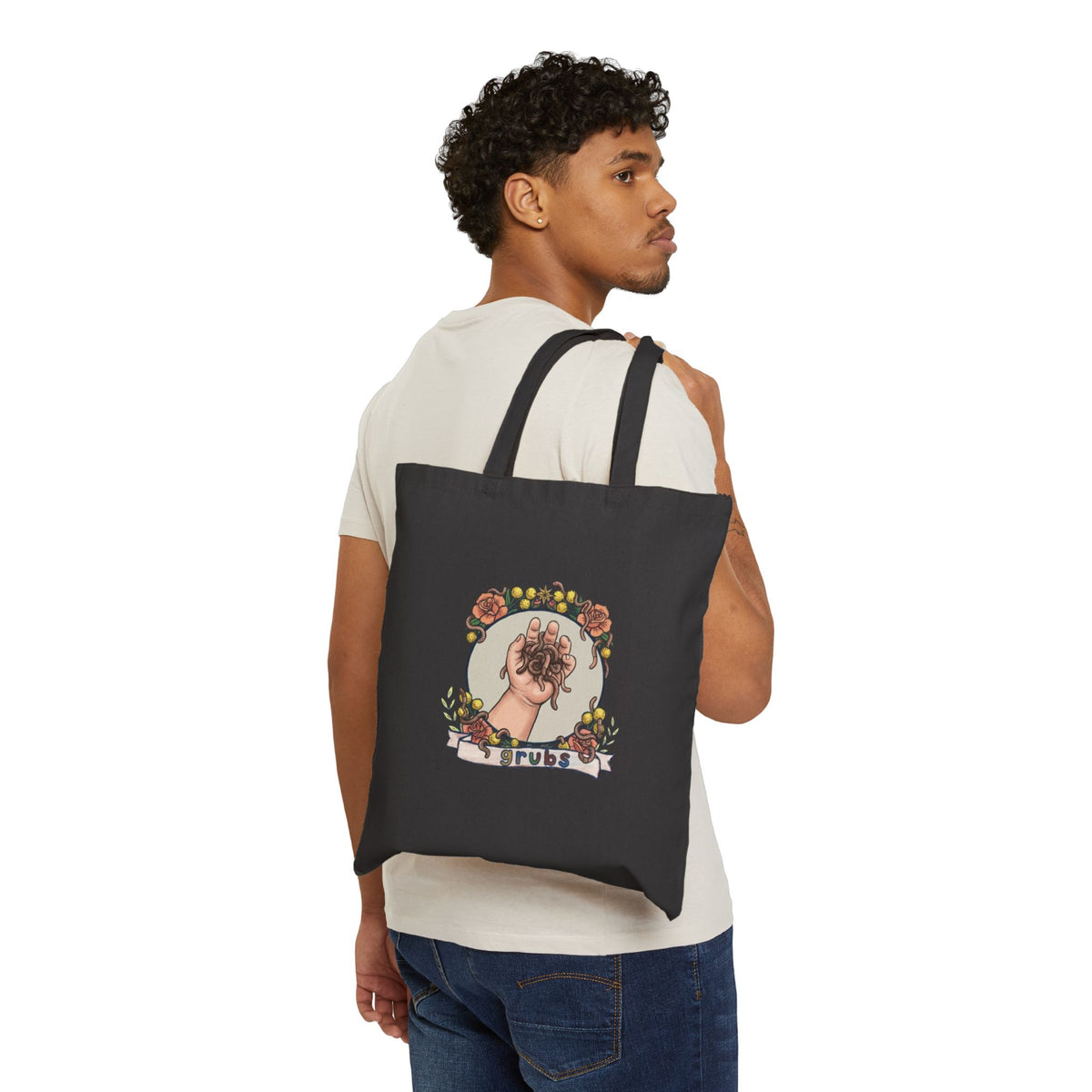 Black canvas tote bag worn by a person, hand-and-grubs graphic on front