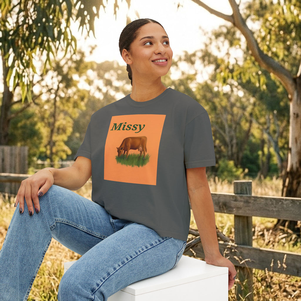 Dark gray boxy T-shirt with orange cow graphic and “Missy” text, model seated.