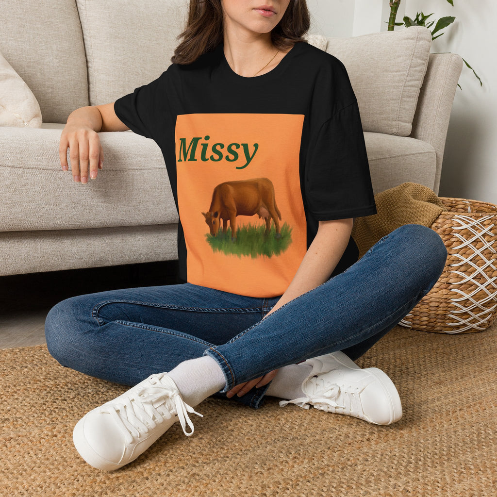 Black cow graphic t-shirt with 'Missy' and grazing cow artwork, seated model view