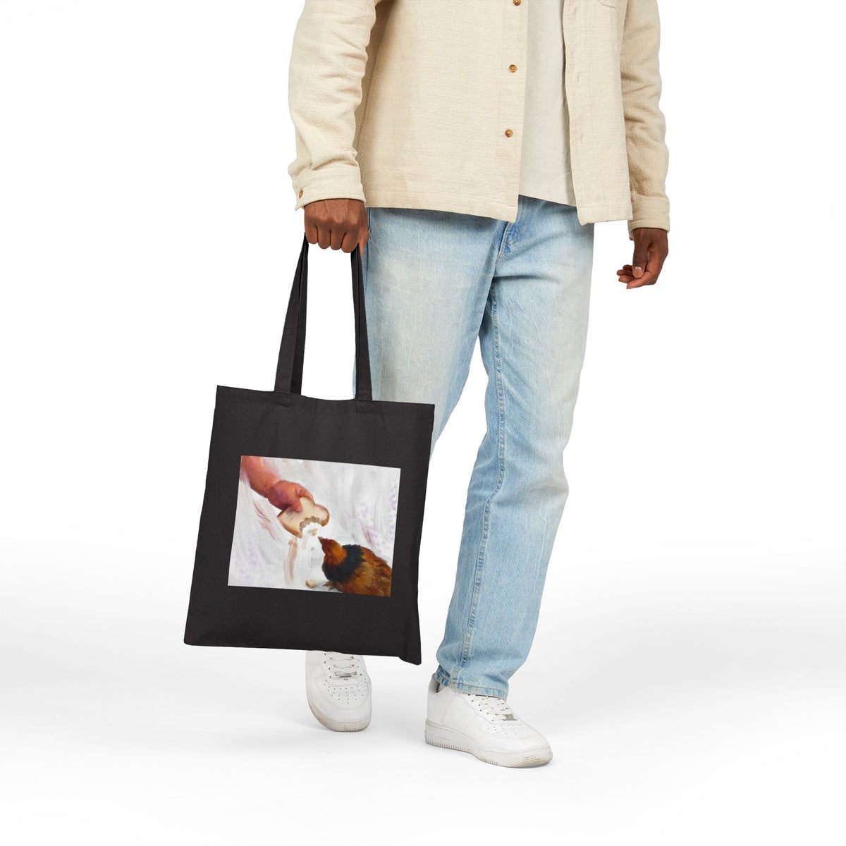 Black canvas tote bag held by a person, with front illustration panel and handles