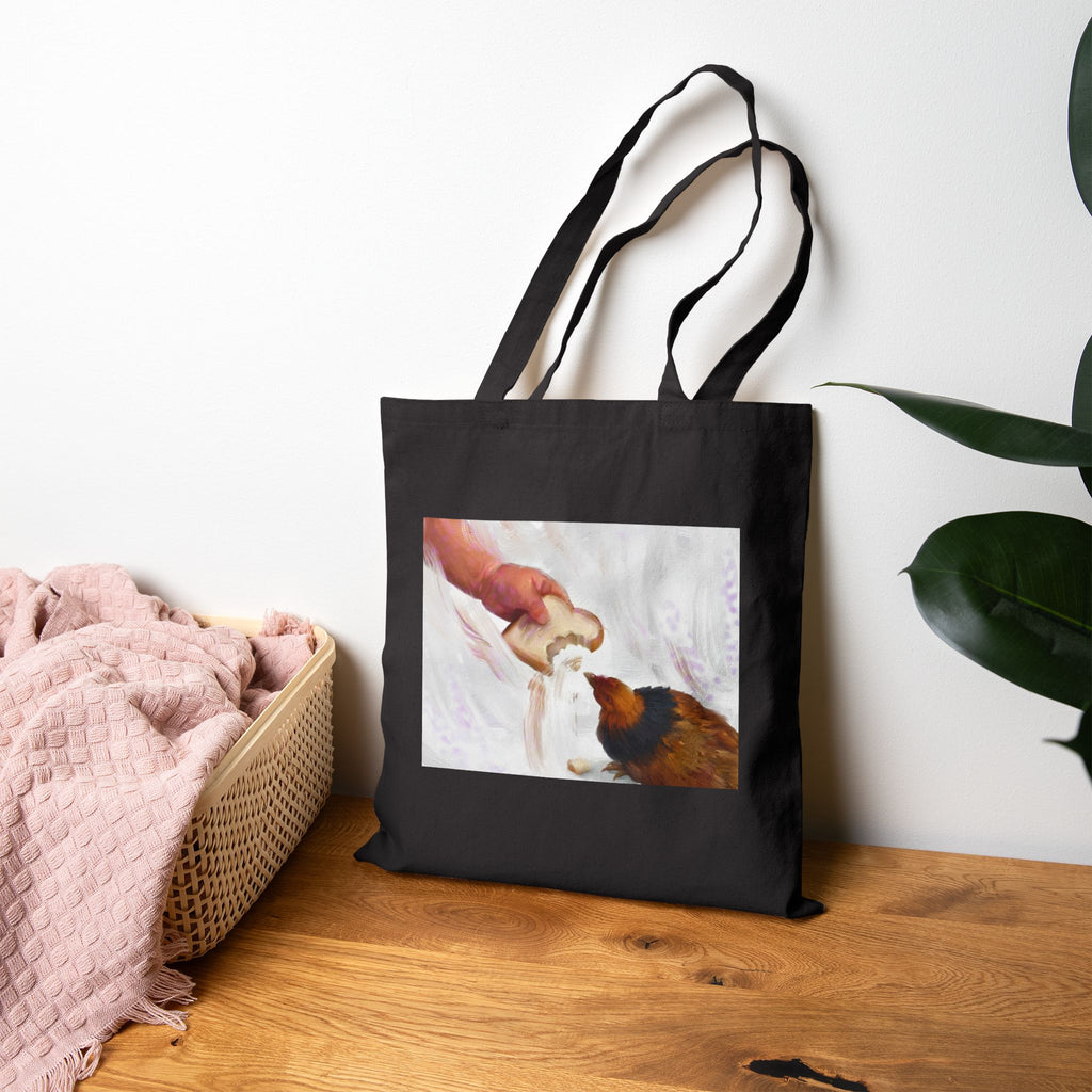 Black canvas tote bag with hen-feeding illustration panel, shown standing upright