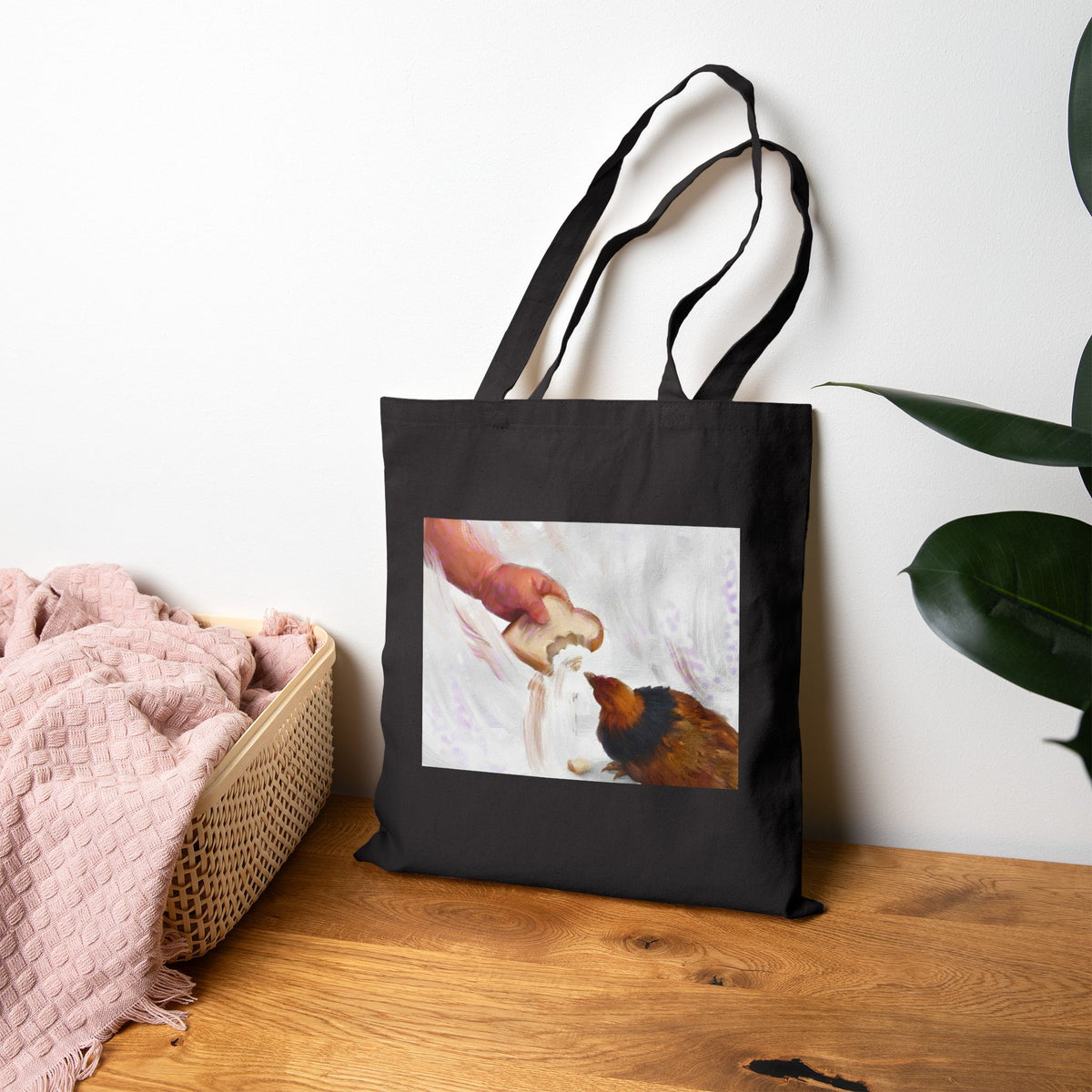 Black canvas tote bag with hen-feeding illustration panel, shown standing upright