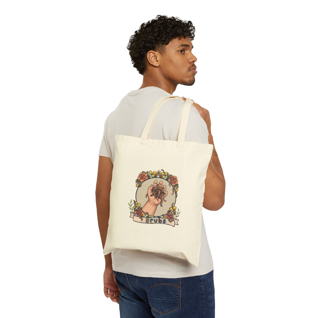 Natural canvas tote bag worn by a person, hand-and-grubs graphic on side