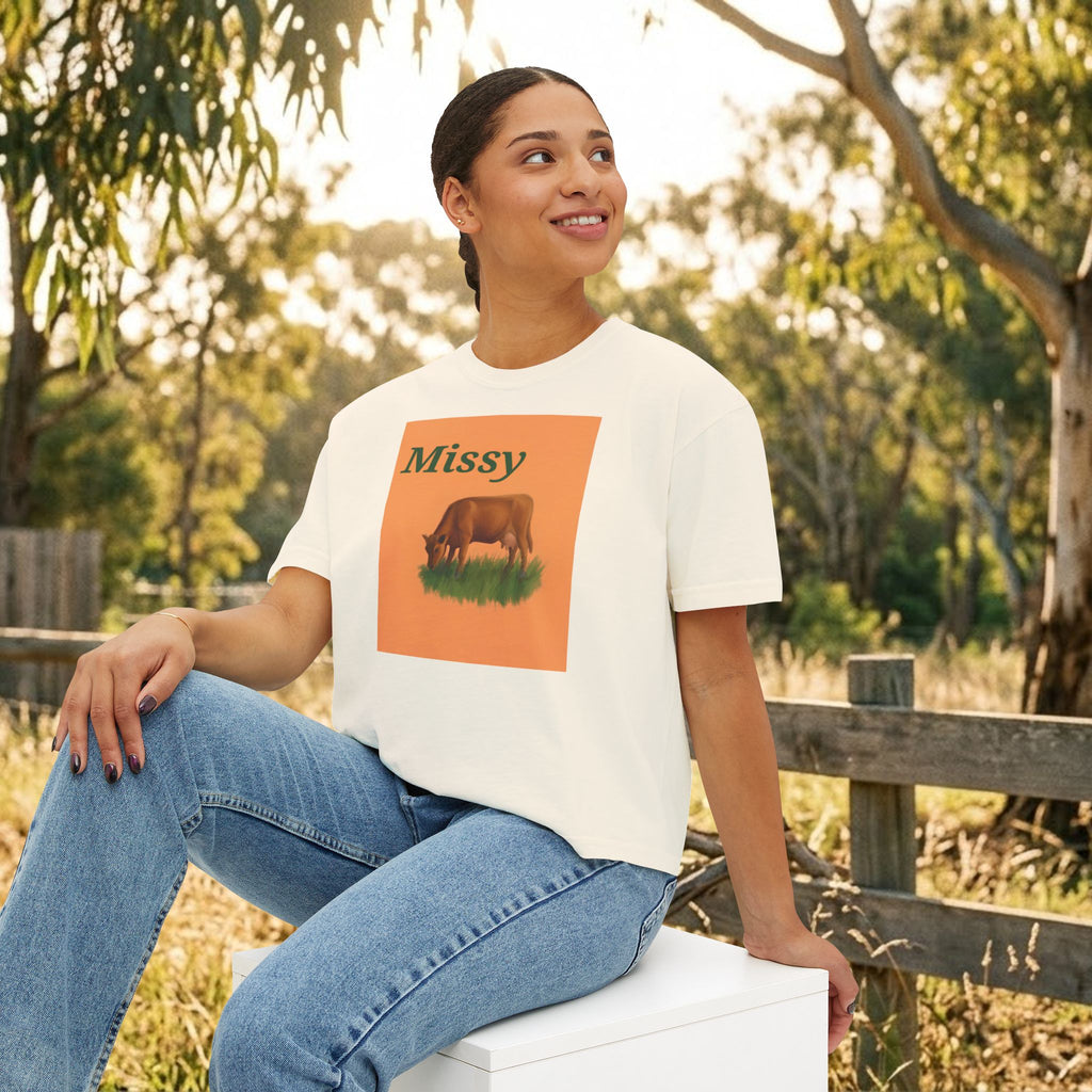 Cream boxy T-shirt with orange cow graphic and “Missy” text, model seated front view.