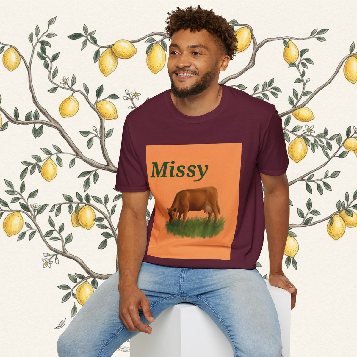 Maroon crewneck T-shirt on model with orange “Missy” graphic and brown grazing cow