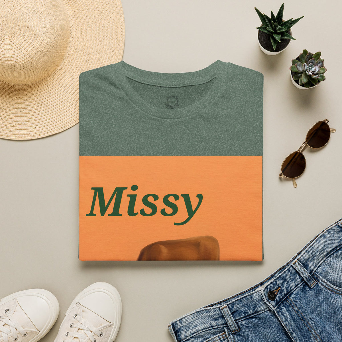 Dark green heather t-shirt flat lay with orange “Missy” grazing cow graphic.