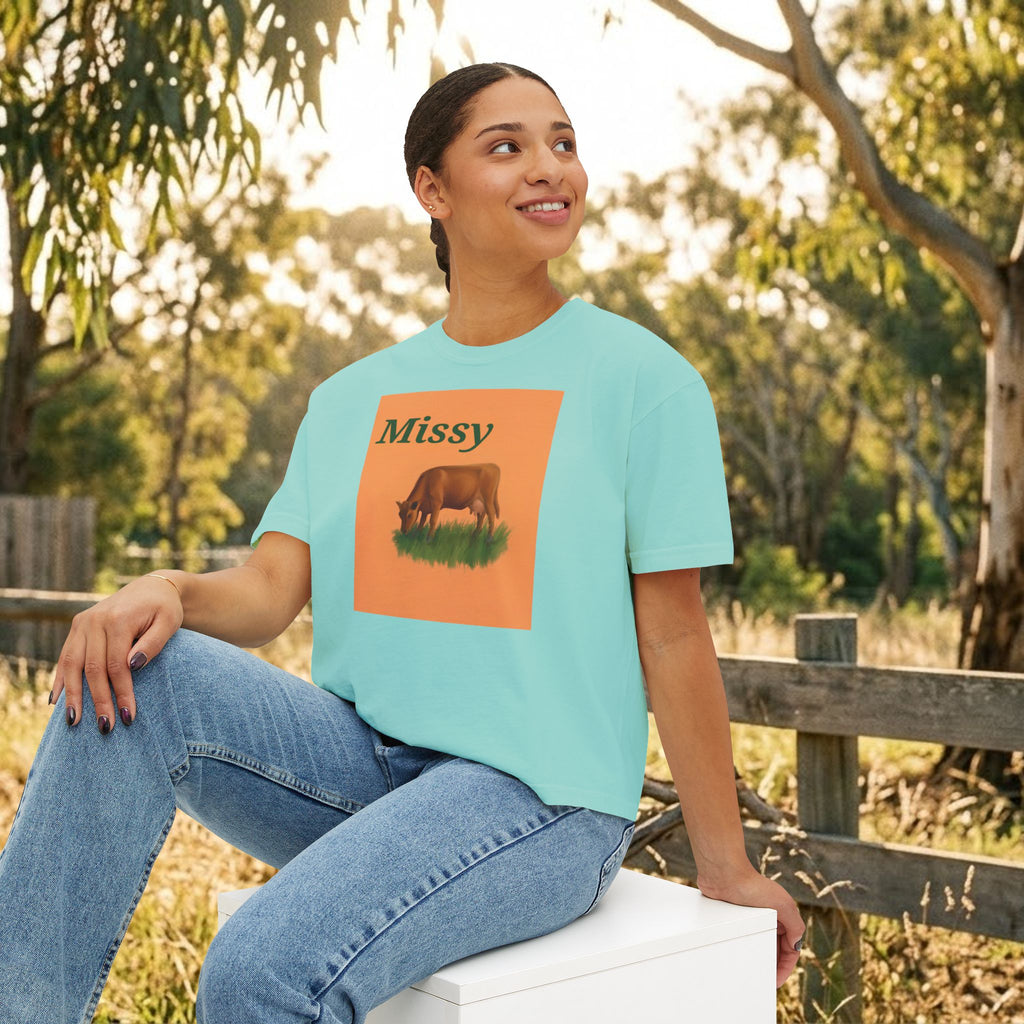 Teal boxy crewneck T-shirt with Missy grazing cow graphic, model seated