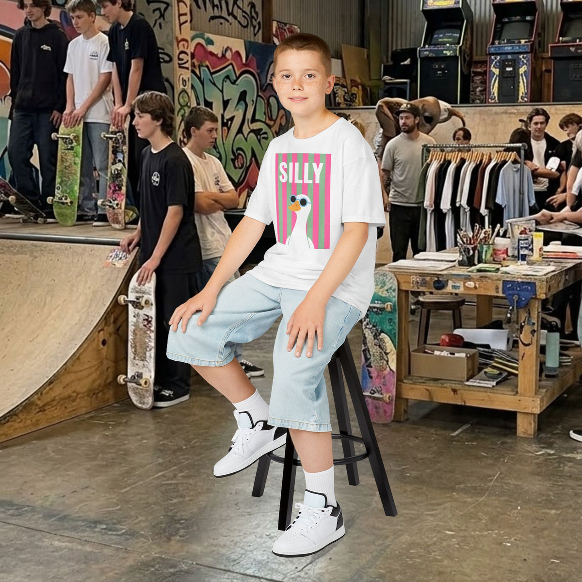 Kids white T-shirt with front “SILLY” duck graphic print, seated on a stool