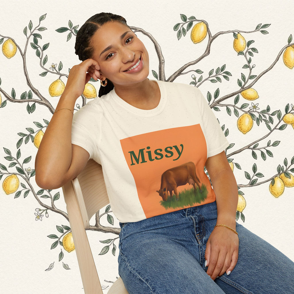 White crew-neck t-shirt showing orange “Missy” grazing cow illustration on front.