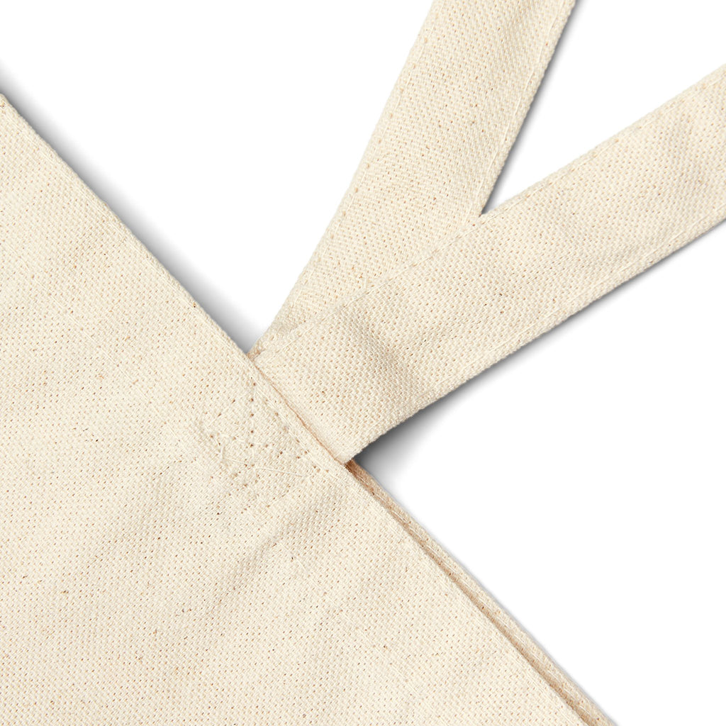 Natural canvas tote bag corner with reinforced seam and top strap attachment.